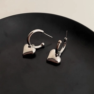 Close-up of silver C-shape hoop earrings with 3D heart charms on a black base