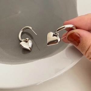 Silver metal heart hoop earrings featuring a polished heart pendant on white ceramic