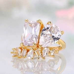 Golden teardrop and emerald cut stone ring set on reflective surface with pave band