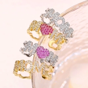 Close-up of MOM letter rings with micro-set zircons and pink heart on wavy metal bands