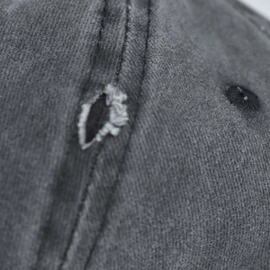 Detailed macro view of washed dark grey cotton baseball cap with distressed hole and stitching