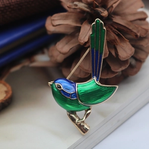 Exquisite enamel bird brooch in green and blue perched on a pine cone backdrop