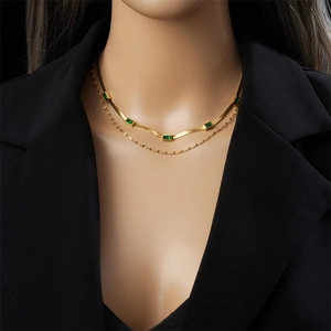 Collana a doppio strato dorata con gemme verdi rettangolari su un blazer nero elegante