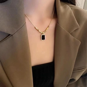 Elegant gold necklace with black square pendant worn by model over a khaki blazer
