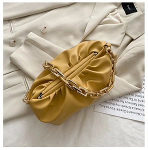 Close-up of bright yellow pleated cloud bag with a chunky gold chain strap on blazer