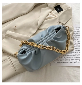 Detail of blue pleated cloud bag featuring premium gold chunky chain on beige blazer
