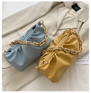Detail of blue and yellow ruched cloud bags with chunky gold chain straps on a beige blazer