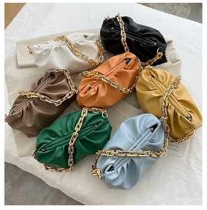 Top view of colorful pleated cloud crossbody bags with chunky gold chains on white fabric