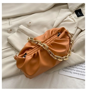 Detail of orange leather cloud bag with ruched texture and thick gold chain strap