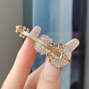 Elegant gold violin brooch with sparkling rhinestones being held to show detail