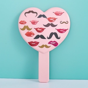 Detailed close-up of a pink heart-shaped handheld mirror with lip and mustache patterns