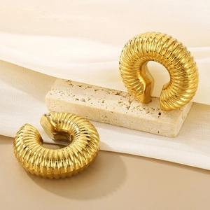 Detail of gold hollow C-shaped earrings with vertical textured stripes on stone stand