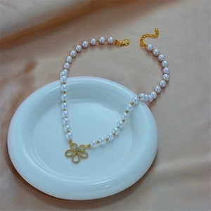 Elegant white pearl necklace with gold flower pendant and crystals on satin background