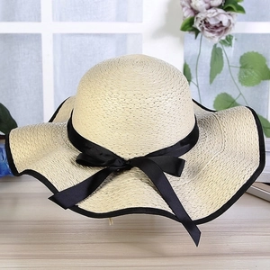 Detailed view of beige straw sun hat with wide brim and elegant black ribbon bow tie