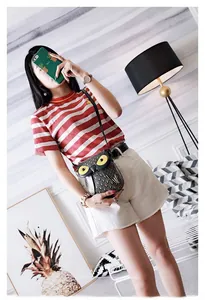 Detailed view of owl-shaped black crossbody bag with yellow eyes on model's outfit