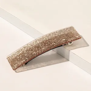 Gros plan d'une pince à cheveux rectangulaire ambrée scintillante sur support blanc