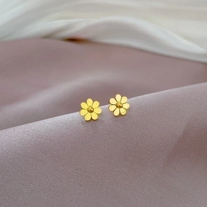 Detail shot of golden floral titanium steel stud earrings on soft textured fabric