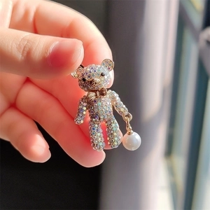 Chic golden bear brooch with colorful rhinestones and pearl pendant held by fingers