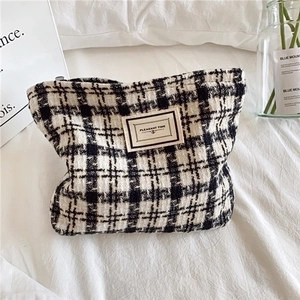 Large plaid tweed makeup bag with checkerboard pattern and zipper on white bedding