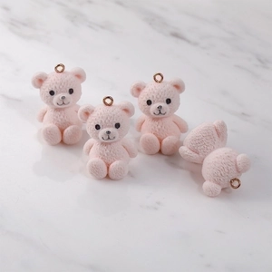 Pink flocked teddy bear pendants with gold rings on a marble background for DIY jewelry