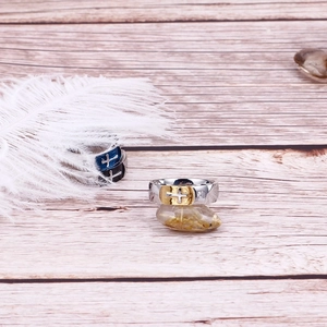 Dettaglio dell'anello con croce e strass su sfondo di legno chiaro e piume bianche