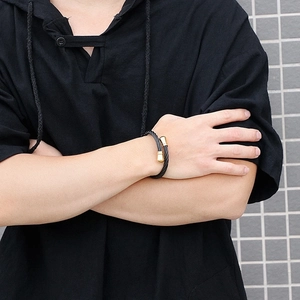 Detail of twisted black cable bracelet with gold-tone cylinder tips on a male wrist