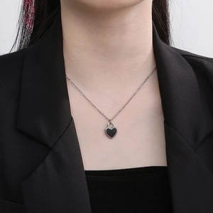 Close-up of a silver chain necklace with a black heart-shaped locket and bead details