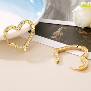 Close-up of golden heart earrings with micro-set cubic zirconia on a floral background