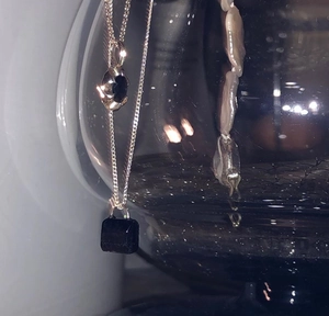 Detail of silver chain with black cube and dark oval gemstone pendant on glassware