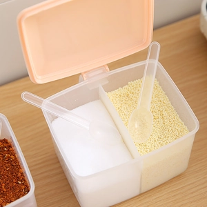 Dual-compartment clear plastic spice box with pink lid and spoons on wooden surface