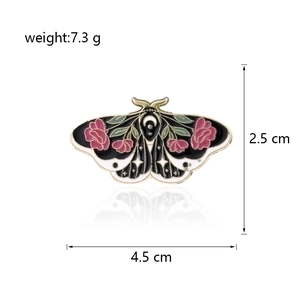 Detailed view of enamel moth brooch with pink roses and star moon patterns on wings