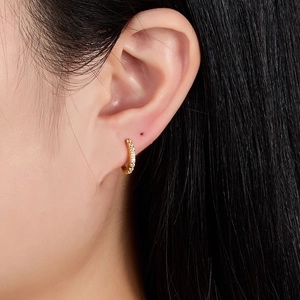Close-up of golden huggie earrings with sparkling clear zircon stones on ear