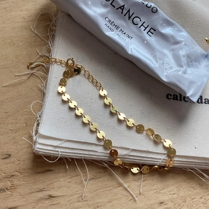 Close-up of minimalist gold disc bracelet on rustic linen fabric background