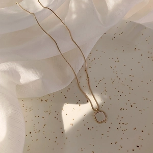 Elegant gold square shell pendant necklace on a textured ceramic plate with white silk