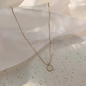 Close-up of gold square shell pendant necklace on elegant white pleated silk background