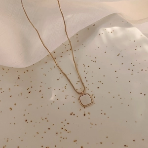 Minimalist square shell pendant necklace with a delicate gold chain on ceramic plate