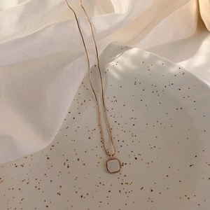 Detailed view of square shell pendant on a gold box chain against white fabric
