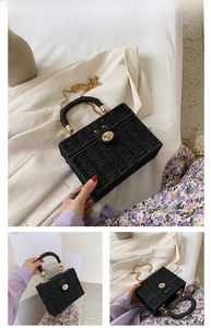 Detail einer schwarzen Stroh-Handtasche mit goldenem Drehverschluss und Metallkette
