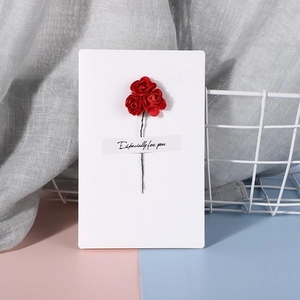 Detailed close-up of handmade white card with three red paper roses and artistic text