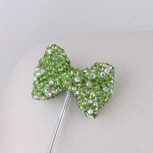 Macro detail of a green rhinestone bowknot charm with sparkling crystals on a silver pin