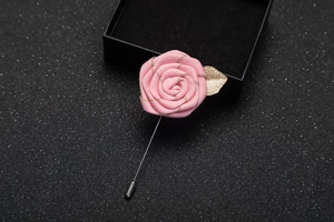 Detail of pink fabric rose brooch with golden leaf and long silver pin for suits