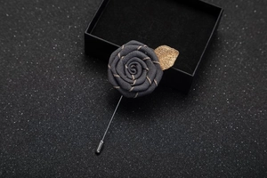 Detail of dark grey fabric rose brooch with gold metal leaf and silver pin on black box
