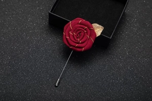 Detailed view of handmade red fabric rose brooch with gold leaves on dark luxury box