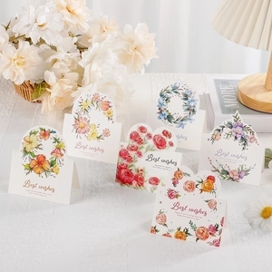 Five assorted 3D floral greeting cards with Best Wishes text on a cozy home desk setup