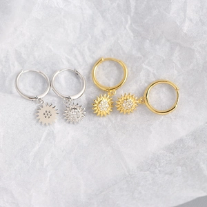 Close-up of gold and silver sunflower huggie hoop earrings on white tissue paper