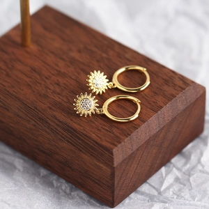 Detailed shot of gold sunflower hoop earrings with clear crystals on a wooden stand