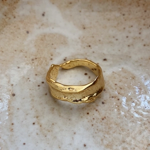 Detail of gold-plated 925 silver irregular lava ring on a beige ceramic surface