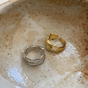 Close-up of irregular textured open rings in gold and silver on a rustic ceramic plate