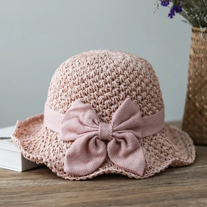 Detailed view of pink woven straw hat with a large decorative bow on a wooden table