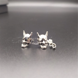 Macro shot of silver punk devil mask stud earrings with matching backings on black surface